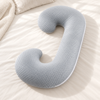 Coussin de grossesse en C gris à picots posé sur un lit